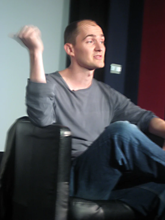 a man holding up a wii remote sitting on top of a chair