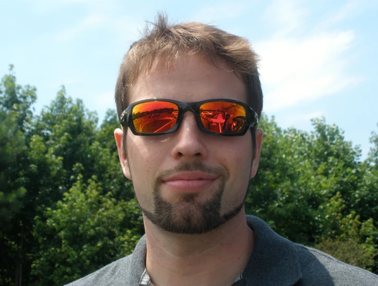 a man wearing red mirrored sunglasses with trees in the background