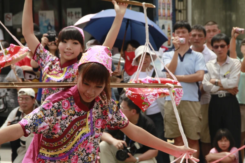 girls with colorful clothing are holding up string poles