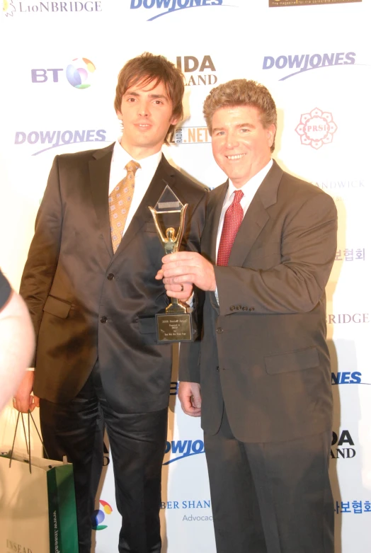 two men dressed in business suits and one is holding a trophy