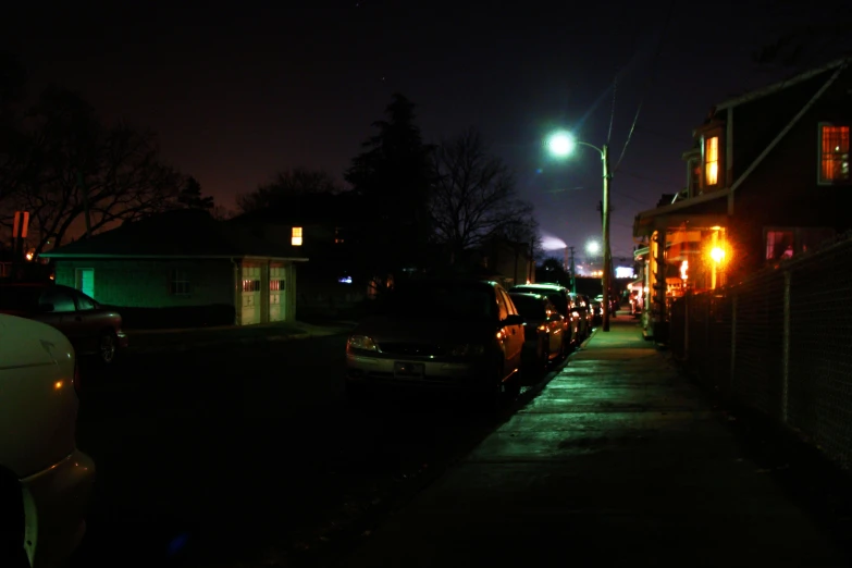 street lamp illuminates on dark night street with cars parked