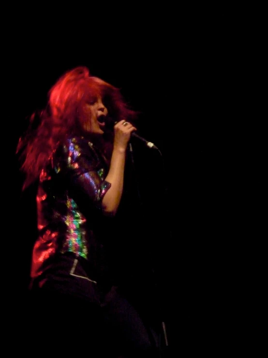 a woman with red hair standing on stage while holding a microphone