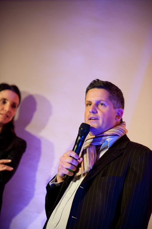 a man speaking into a microphone while another man watches