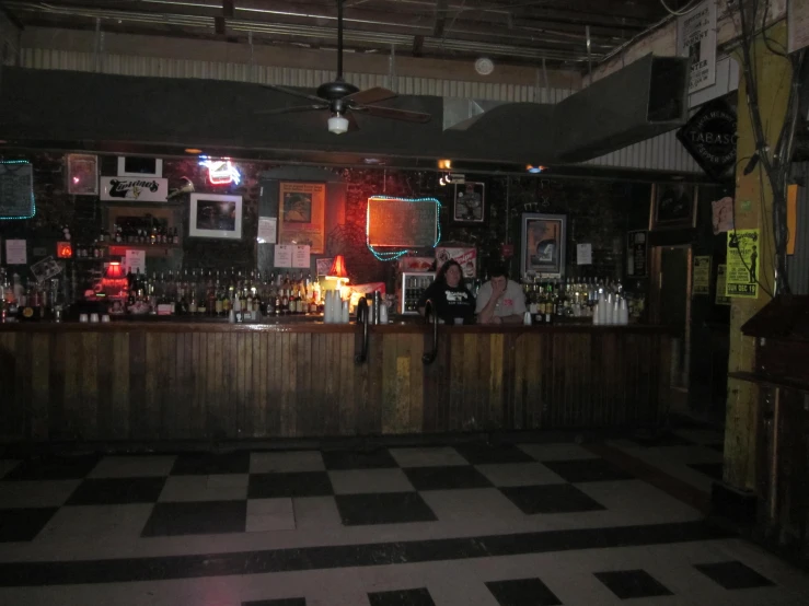 a checkered floor is in front of a bar with a wall of bottles and pictures