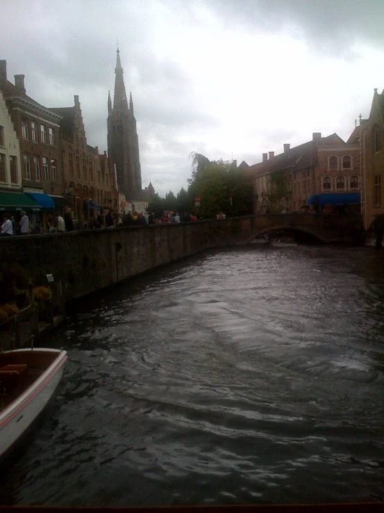 a boat is traveling down a river as people are walking by on the sidewalk and around the building