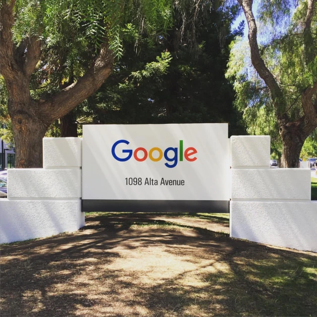 there is a large google sign located under trees