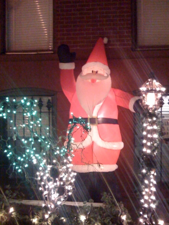 lighted santa clause figure standing near shrub with wreath on back of house