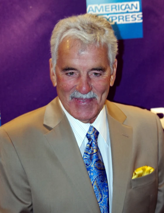 man with grey hair and a mustache standing next to a purple backdrop