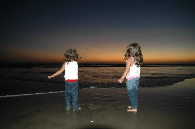 two little girls standing on the beach watching the sun set