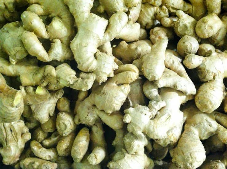 a pile of sliced up ginger with lots of heads of fruit in the background