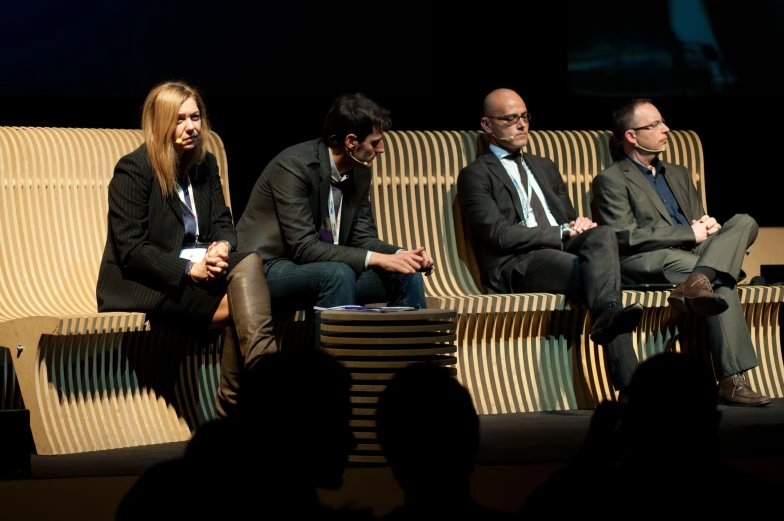 four people in business suits sit on benches with shadows on the wall