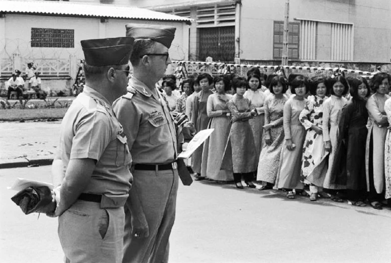 a man in uniform talking to a man in front of a large group of women