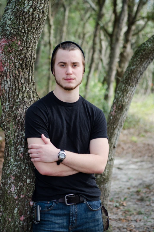 young man standing next to a tree in the woods