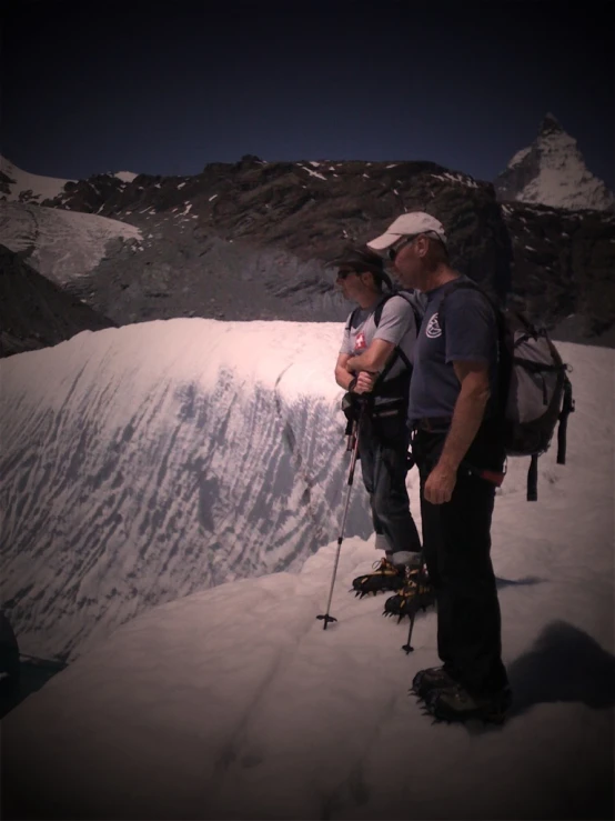 two people wearing backpacks and skis on a mountain