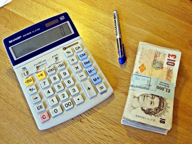 a calculator and pen sit beside one large bank note