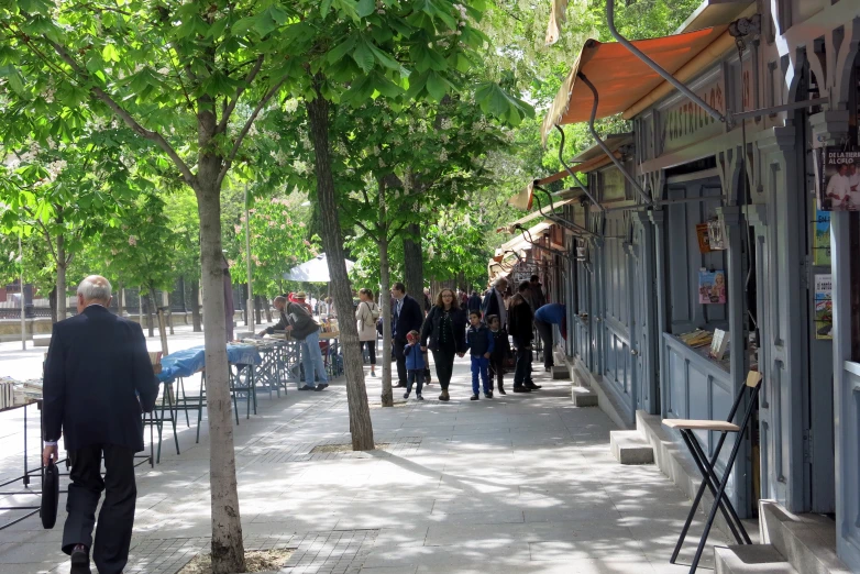 many people walk on the sidewalk near businesses