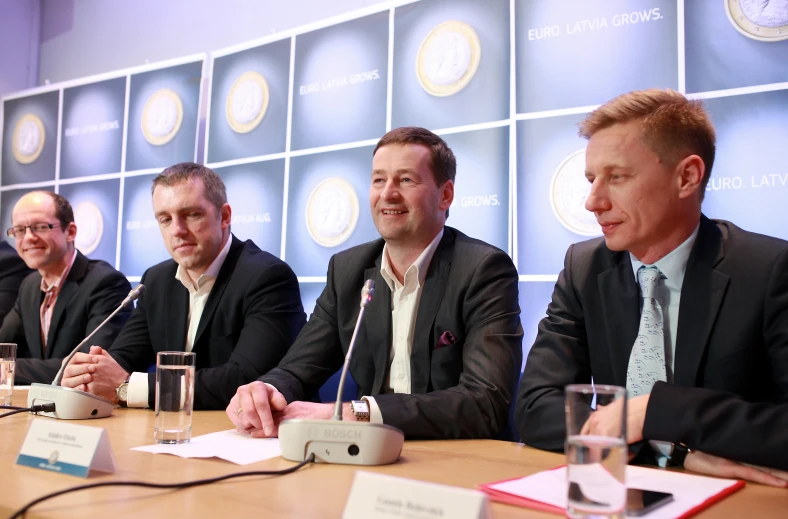 four men are sitting at a table listening to speakers