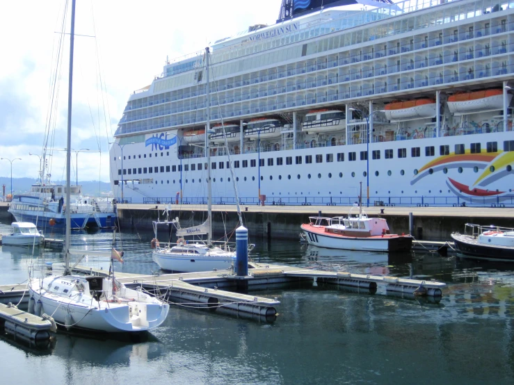 several sailboats in a dock, with a cruise ship in the background