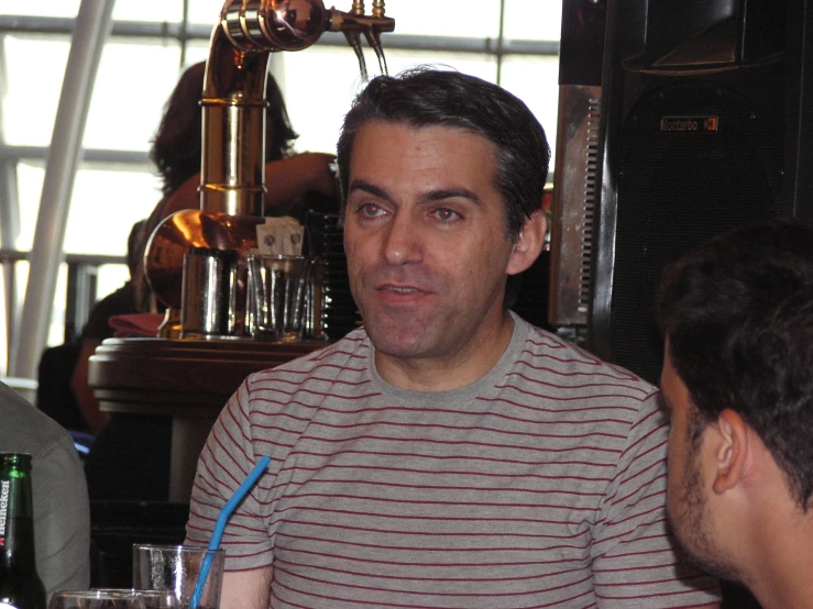 man talking in a bar with another man holding a beer