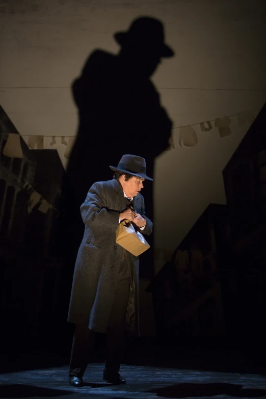 a man in a hat, coat and topcoat standing against a wall