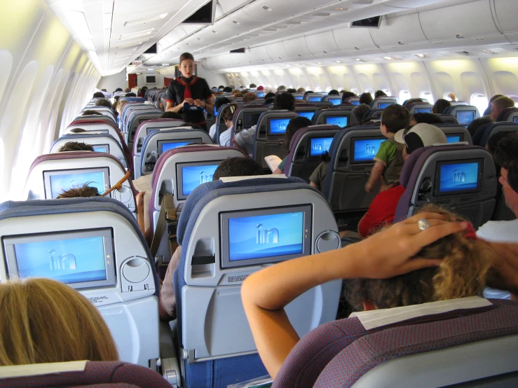 a crowd of people sit in chairs while some look at monitors