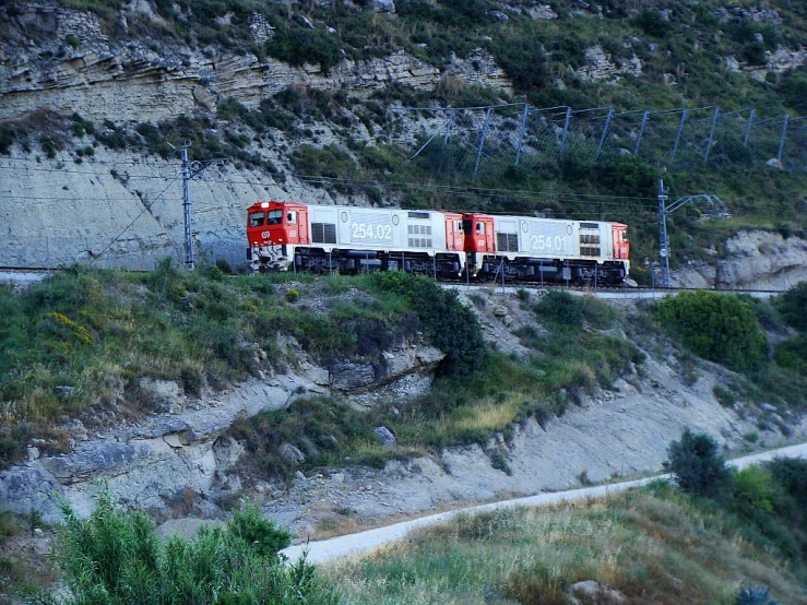 a train traveling along the tracks along a rocky hill