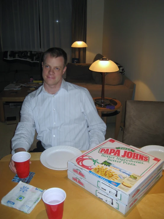 man sitting in front of pizza boxes with cups on a table