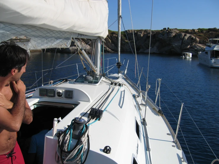 the man is talking on his cellphone while he sits on the deck of a sailboat