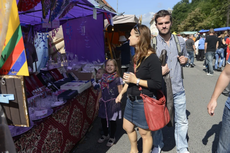 people are walking around a vendor stand, some in dark clothing and the others wearing pink