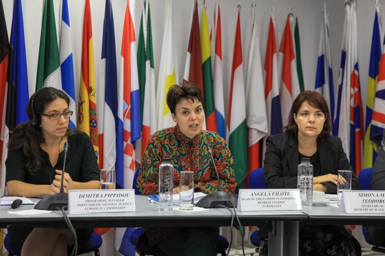 three women sitting at a table, each with their hands folded in front of them