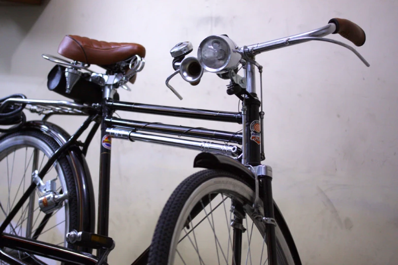 a black bicycle with a brown saddle sitting against a wall