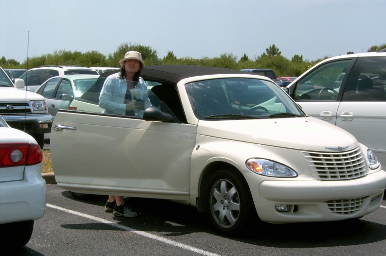 a woman with an odd hat stands in front of a very nice looking car