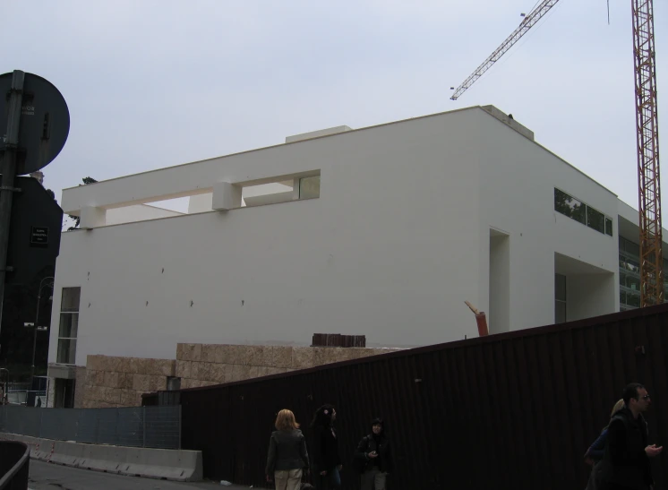 people walk near a tall white building under construction