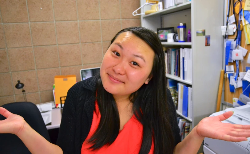 a lady with long hair holds out her hand in front of an office desk