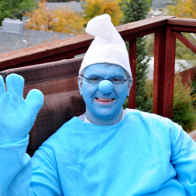 blue man with glasses and a silly face holding up a peace sign