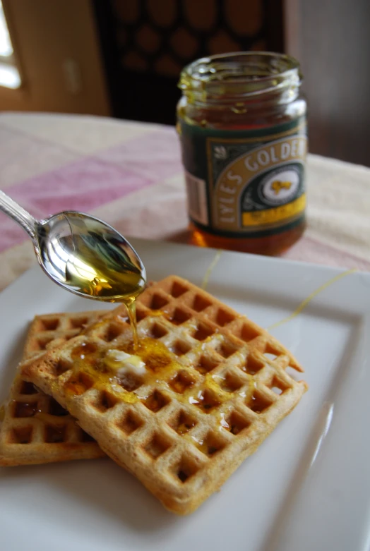 two waffles, a spoon and honey sitting on a plate