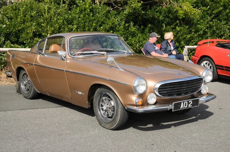 people sitting in an old fashioned car and a red car