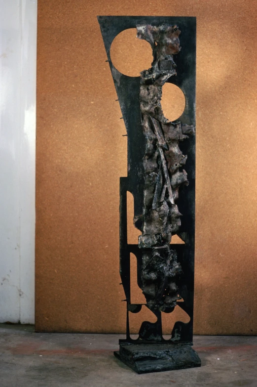 a tall metal sculpture on display near a brown wall