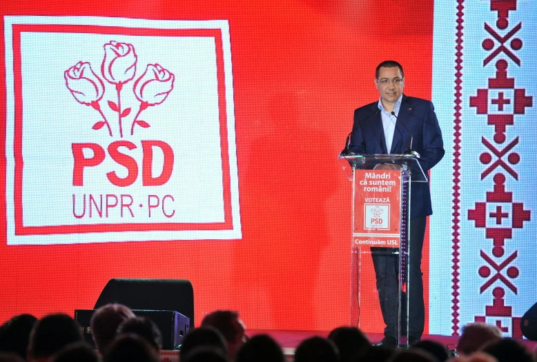 a man at a podium in front of red banners