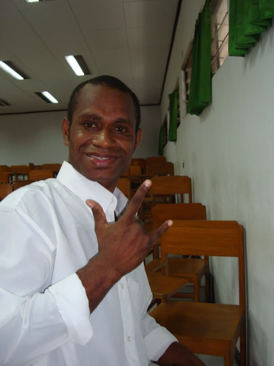 a man in white shirt and black tie standing next to rows of wooden chairs