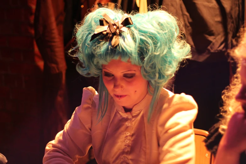 a lady with turquoise hair and blue bangs looks down at a note