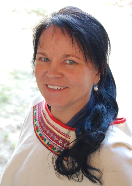 woman with blue hair and an ornate necklace smiling