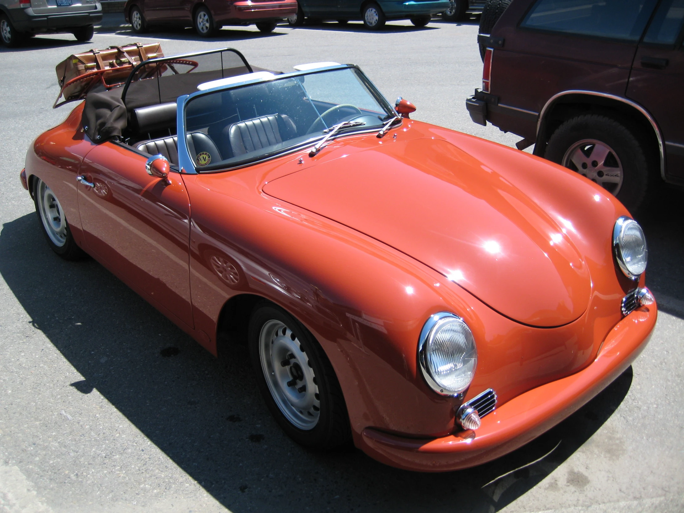 an orange car sitting in a parking lot with two luggage bags on top of it