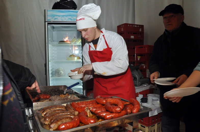 man in an apron prepares  dogs from an open refrigerator