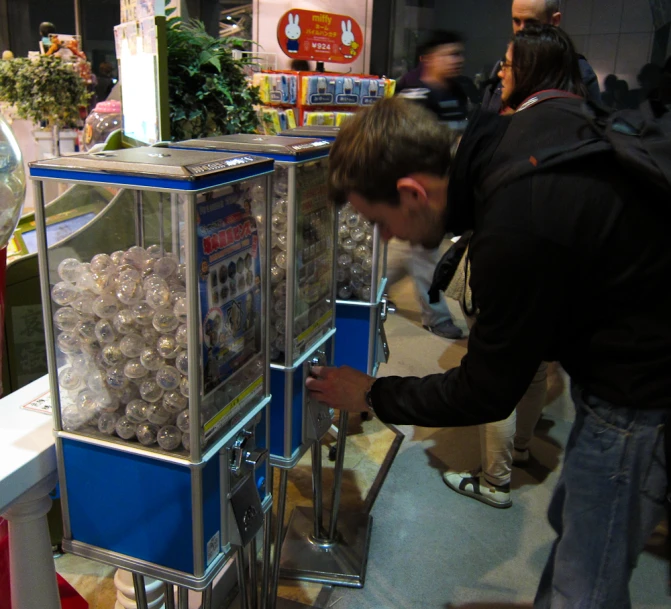 the young man is looking at a machine that has many balls of food in it