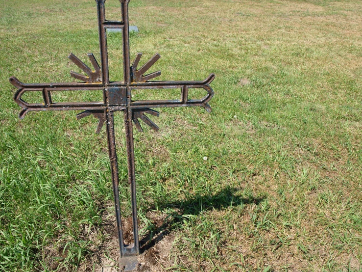 a metal cross standing in the grass in the middle of a field