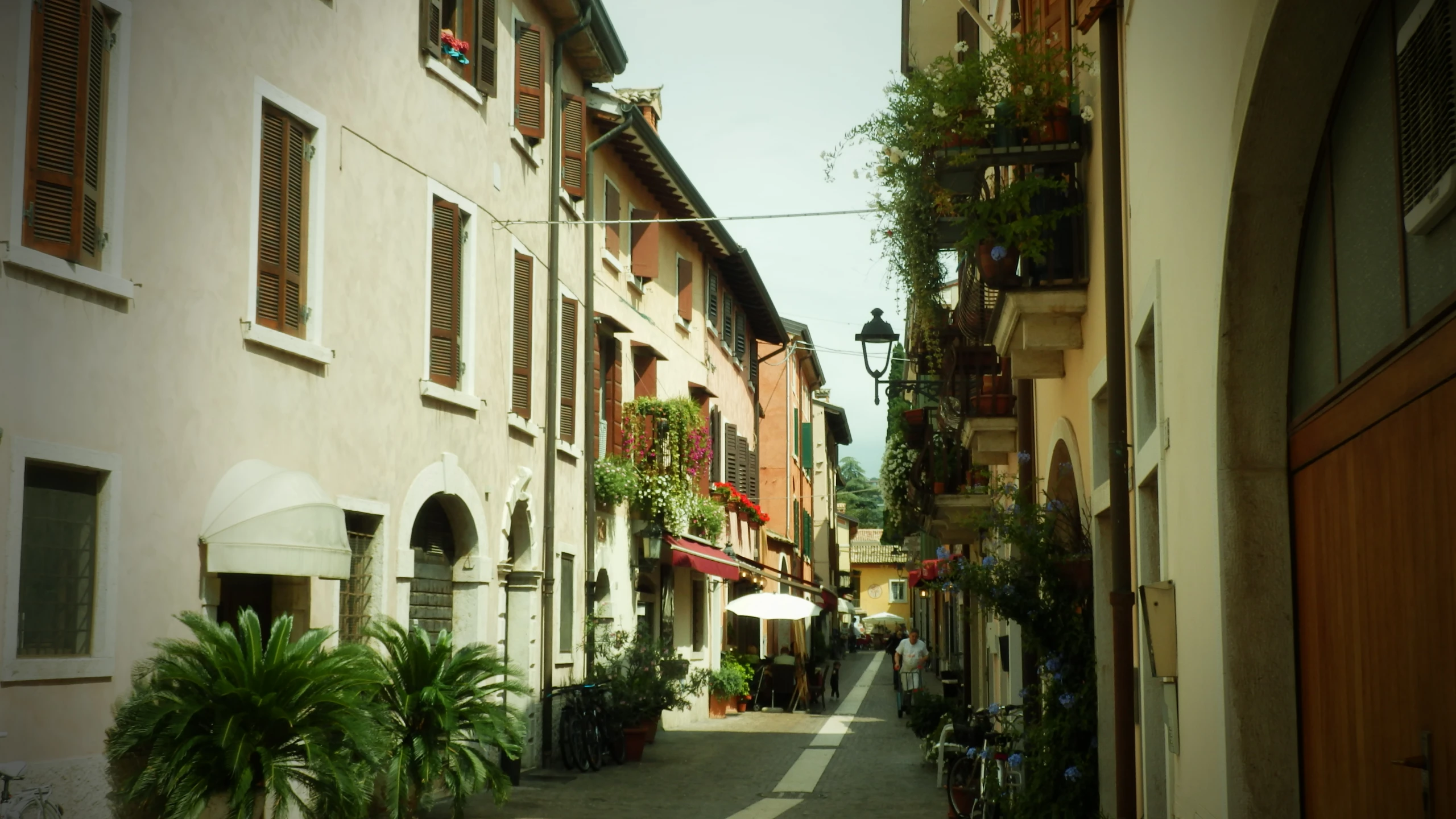 an alley leading into a city with buildings and flowers on display