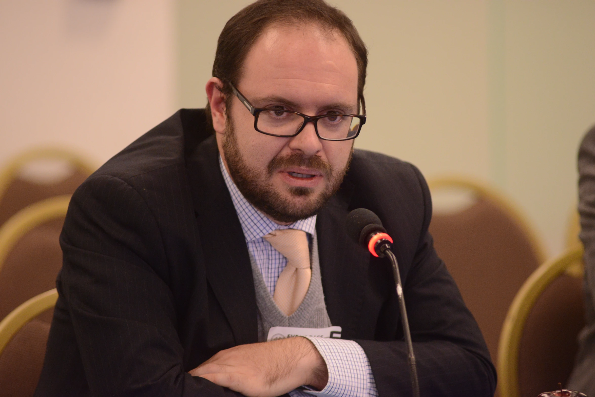 a man with glasses sitting at a table in front of a microphone