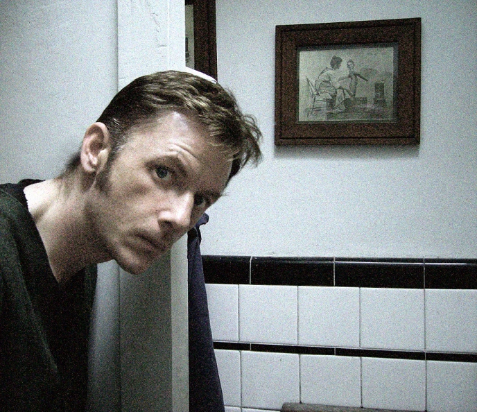 a man in the middle of bathroom with a hand on his chest