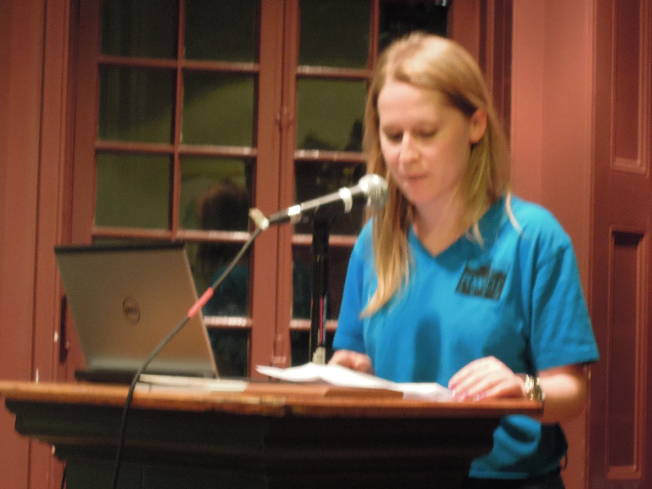a woman standing in front of a microphone, writing at a desk